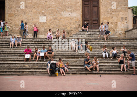 Tourists sitting and relaxing on the steps of Duomo (Cathedral) in Piazza del Duomo (Cathedral Square) in hilltop town of San Gimignano, Tuscany, Ital Stock Photo