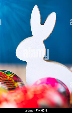 Easter bunny figurine with colorful eggs. Warm sunlight flare. Blue background. Stock Photo