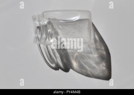 Highlighted Empty Plastic Jar And Its Shadow. Pet Plastic Jar left in the closed car in the high summer heat distorted its shape, white background Stock Photo