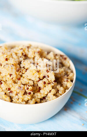 closeup of a white ceramic bowl with cooked quinoa, on a rusti pale blue wooden table Stock Photo
