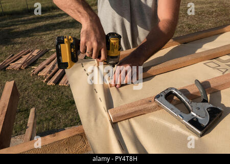 Roof construction building. Man using electrical scredriver to attach construction elements. Stock Photo