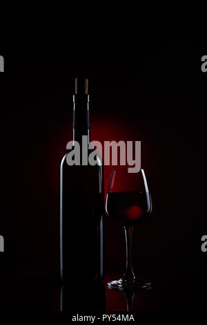 A bottle of red wine with a half full wine glass using stripbox for rim light effect Stock Photo