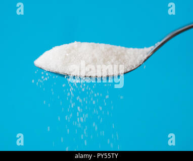 Sugar being pour from a spoon in a stream isolated on blue background in Too much sugar Sweet addiction diabetes disease unhealthy food concept. Stock Photo