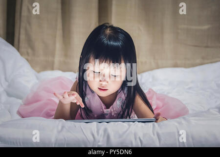 Little girl lying tablet on bed at night using the internet watching vdo or gamp play Children Smartphone or tablet Addiction concept. Stock Photo