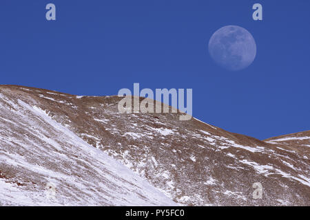 Moon rises over rocky mountains in winter near sunset Stock Photo