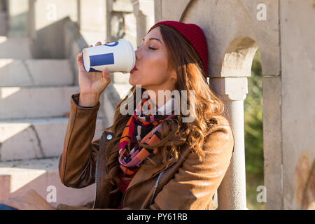 Beutiful young woman drinking coffee to go in a park sitting on stairs Stock Photo