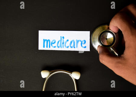 Conceptual image with Medicare inscription with the view of stethoscope, in someone hand with black background. Medical Conceptual. Stock Photo