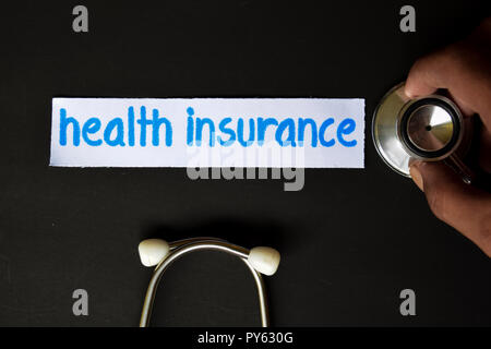 Conceptual image with Health insurance inscription with the view of stethoscope, in someone hand with black background. Medical Conceptual. Stock Photo