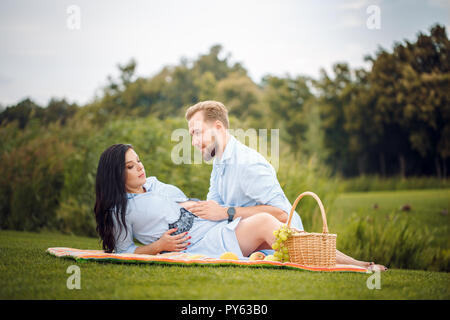 young couple having a picnic in a city park, a woman is expecting a baby. Stock Photo