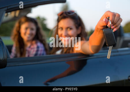 Beautiful young woman reaching out car keys to the camera while smiling at the camera Stock Photo