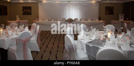 wedding reception room in a hotel with round guest tables with white tablecloth and pink ribbons on chairs Stock Photo