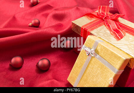 Two gift boxes with bows, on red wavy satin fabric with Christmas balls. Stock Photo