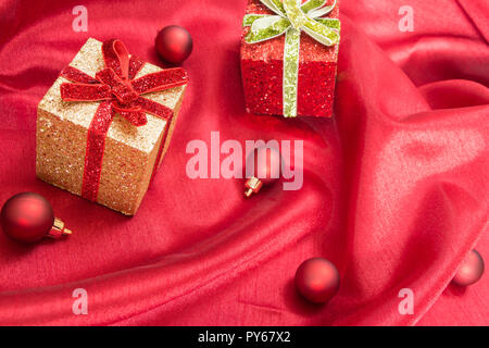 Two gift boxes with bows, on red wavy satin fabric with Christmas balls. Stock Photo