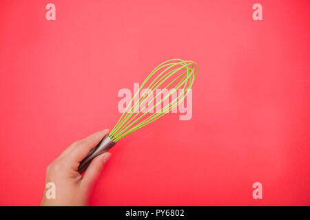 whisk for whipping eggs in female hand on red background. Stock Photo