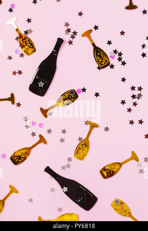 Party confetti background in black and gold colors. There are small bottles of champagne with golden glasses and silver stars on pink background. Festive concept. Stock Photo