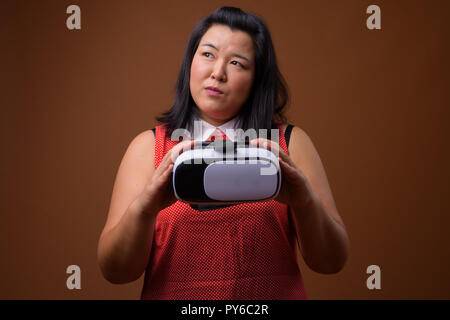 Beautiful overweight Asian woman using virtual reality VR glasses while thinking Stock Photo