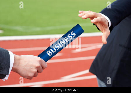 Close-up of two businessman's hand passing a blue relay baton in stadium Stock Photo