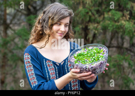 Young woman outside, outdoors, holding glass bowl of homemade red, purple cabbage salad dish with green onions, scallions Stock Photo