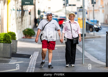 Rome, Italy - September 4, 2018: Happy couple tourists walking in city town sidewalk with Roma hat, holding hands Stock Photo