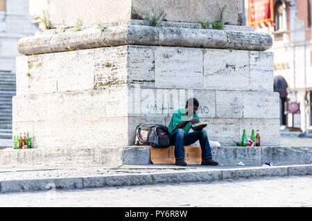Rome, Italy - September 4, 2018: African refugee homeless man sitting in city park eating food by Obelisco Esquilino in piazza square Stock Photo