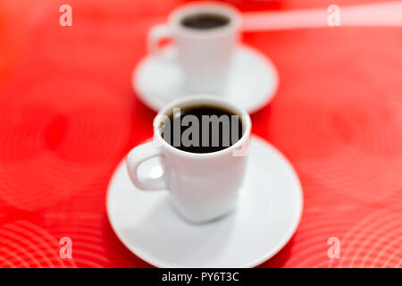 Macro closeup of two espresso dark roast coffee cups with detail, texture of black brown liquid on plate, red background table in Italy cafe breakfast Stock Photo