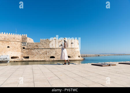 Happy tourist woman relaxing at the Venetian port of Heraklion. Lovely stylish girl arms outstretched  enjoyes vacation travel to Crete. Girl on sight Stock Photo