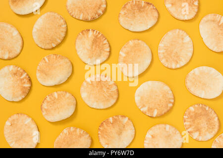 Lots of freshly baked mini pita bread on bright yellow background. Stock Photo