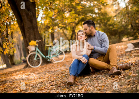 Cheerfull young couple sitting on ground in autumn park Stock Photo