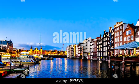 Night scene of the row of historic houses along the Damrak canal, dating back to the 18th century, in the historic center of Amsterdam in Holland Stock Photo
