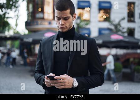 Businessman texting. Serious young businessman holding mobile phone and looking at it outdoors Stock Photo