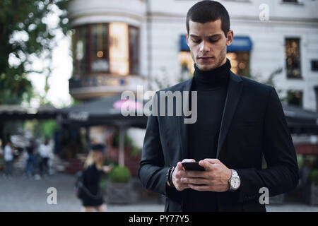 Businessman texting. Serious young businessman holding mobile phone and looking at it outdoors Stock Photo