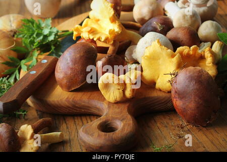 Mix of forest mushrooms on cutting board over old wooden table Stock Photo