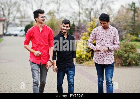 Three indian guys students friends walking on street and looking at mobile phone. Stock Photo