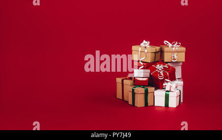 Pile of christmas gift boxes isolated on a red background. Colorful gift boxes tied with ribbons and bows. Stock Photo