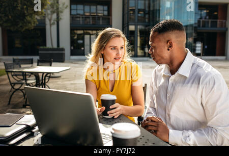 Two business people talking while sitting at office cafeteria. business woman with man sitting outdoors at a table discussing work. Stock Photo