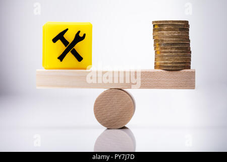 Yellow Under Construction Icon Cubic Block And Stacked Coins Balancing On Wooden Seesaw Stock Photo