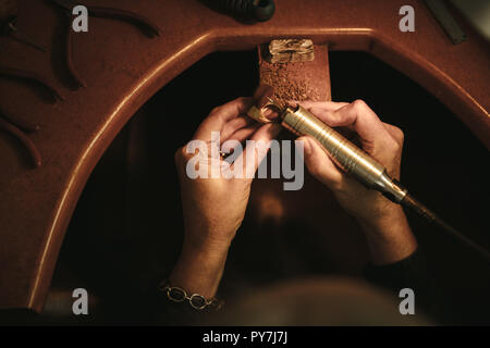 Close up of female jeweler hands polishing a ring at her workbench. Goldsmith making ring surface seamless with grinding machine at workshop. POV shot Stock Photo