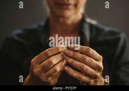 Close up of female jeweler hands examining ring at workshop. Focus on woman jewelry maker hands inspecting a silver ring. Stock Photo