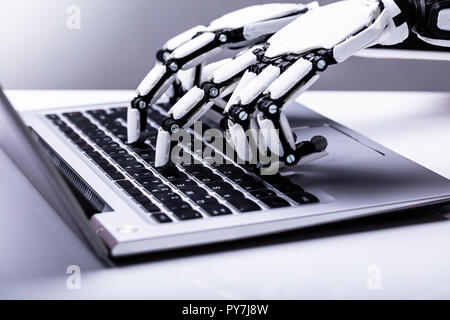 Close-up Of A Robotic Hand Using Laptop Over Desk Stock Photo