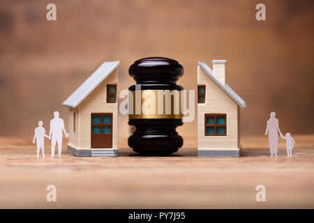 Close-up Of Gavel Between Split Family Figures And House Model On Wooden Desk Stock Photo