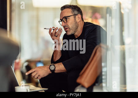 Mature businessman sitting in the hotel lobby with laptop making phone call. Male entrepreneur sitting in hotel waiting area making call. Stock Photo