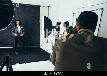 Photographer shooting photos of a model in a studio with his crew holding studio flash lights. Stock Photo