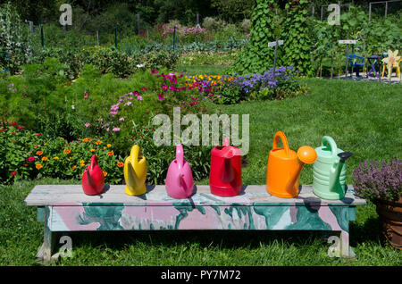 Row of colorful watering cans on painted bench in garden, Community Garden, Maine, USA Stock Photo