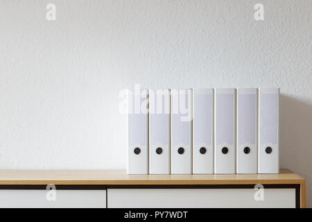 White file folders on wooden sideboard in modern bright office Stock Photo