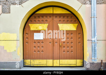 A closed grunge brown wood old door with decorative embossed round elements and gold metal plates with nails. A wood gate inside stone arch Stock Photo
