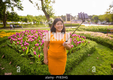 Asian woman taking selfie with mobile phone attach to selfie stick in park Stock Photo