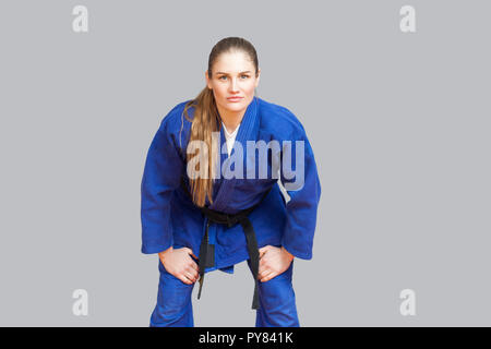 Beautiful athletic karate woman in blue kimono with black belt in fighting stance are looking at camera. Japanese martial arts concept. Indoor, studio