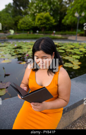 Beautiful overweight Asian woman reading book in park Stock Photo