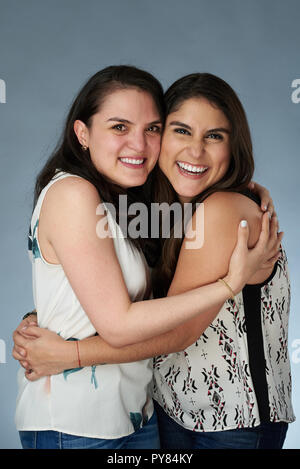 Two happy smiling latino girls hugging on gray studio background Stock Photo