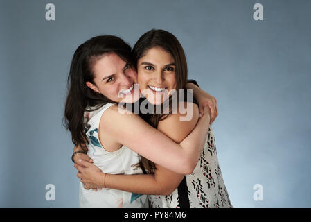 Two young smiling girl friends hugging on studio background Stock Photo